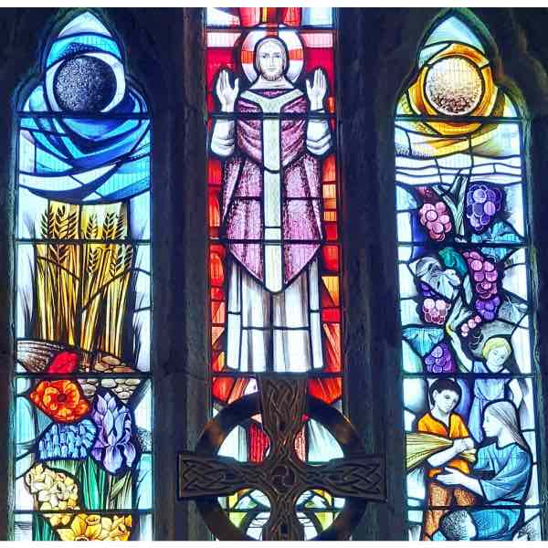 colourful triptych stained glass window plus celtic cross above the altar in Tintagel Church, aka St Materiana, in Cornwall.