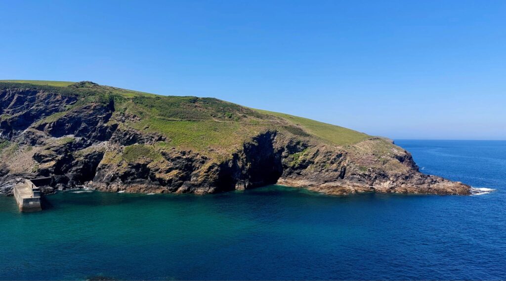 a green rocky headland in deep blue sea and sky