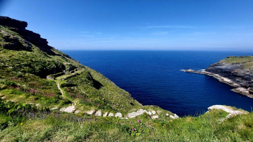 Grassy slopes and headland in deep blue sea and sky with an old stone pathway