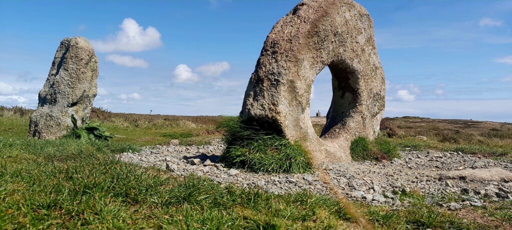 a ruined engine house seen through the centre of the stone with a hole in it at Men an Tol in West Cornwall