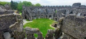 a view into a ruined circular stone castle with grassy floor and trees behind
